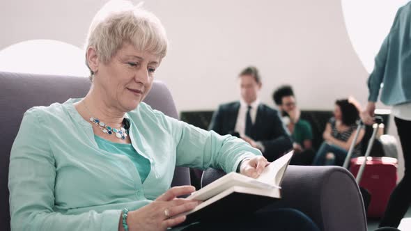 Senior adult woman reading book in airport waiting lounge