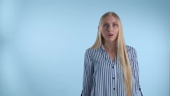 Blonde Young Woman Spreading Her Hands to the Sides and Saying "What" on Blue Background alt