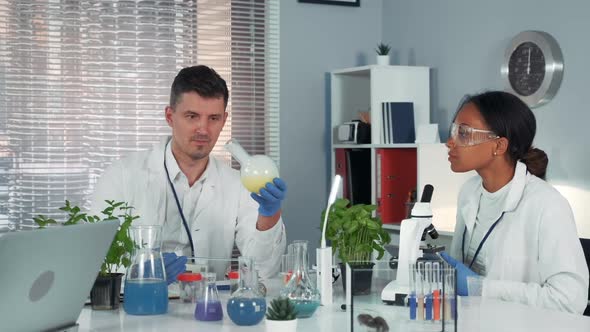 Research Scientist Providing Experiment with Liquid in Flask While His Collegue Observing the alt