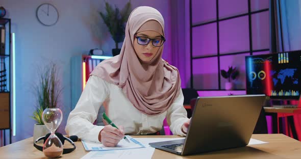 Arabian Businesswoman in Hijab Checking Information on Laptop Screen with Datas on Financial reports alt
