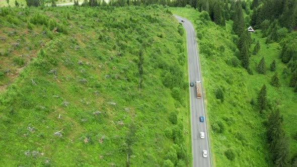 Aerial View of the Road with Driving Cars and Truck in the Mountains with High Green Fir Foliar Pine alt