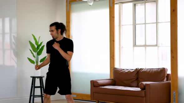 Latino Man with Ponytail and Goatee Performing Taekwondo Axe Kicks Back and Forth in Home alt