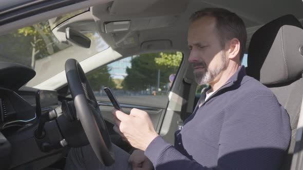 A Middleaged Handsome Caucasian Man Works on a Smartphone Then Looks at the Camera in His Car