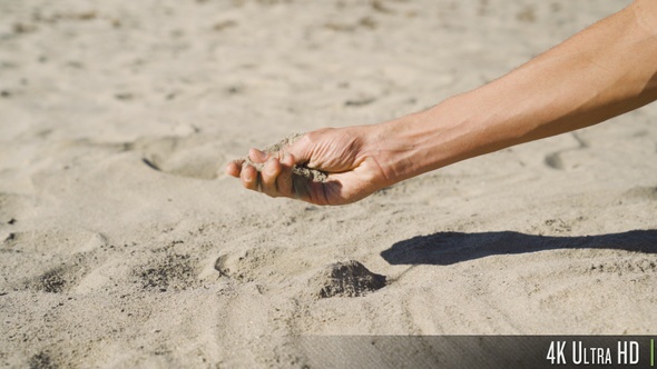 4K Picking up a handful of sand and moving it through his fingers alt
