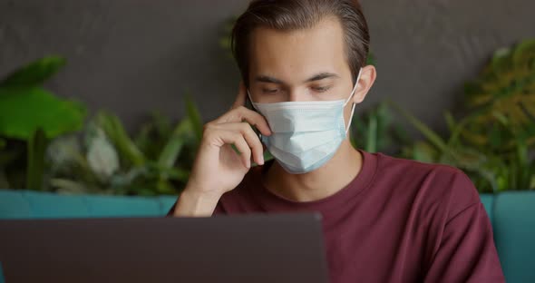 Handsome Man in Street Cafe Working on Laptop and Talking on Mobile Phone Wearing Mask During alt
