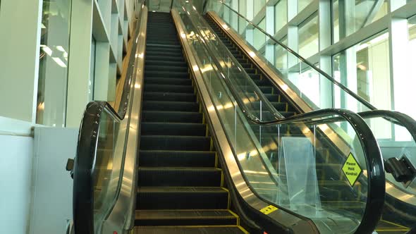 Empty escalators going up and down with windows to look out on a bright sunny day.