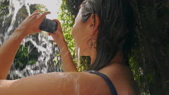 Beautiful Asian Girl in Blue Swimsuit Shooting Video on Modern Fashionable Phone Against Backdrop