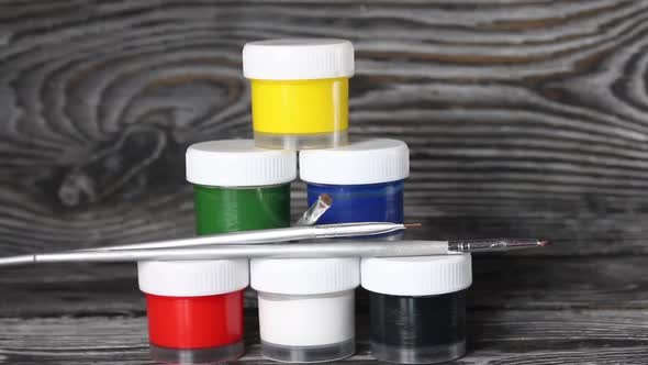 A Set Of Gouache And Brushes. Jars Of Paint Stand In A Pyramid.  Slider Camera. On Pine Boards