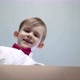 Happy Little Blond Boy in a White Shirt with a Red Bow Tie Opens a Cardboard Box and Smiles - VideoHive Item for Sale