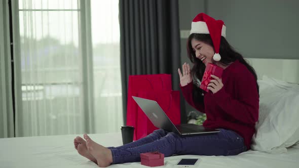 happy woman using laptop computer and holding Christmas gift on a bed