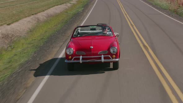 Tracking shot of man driving classic convertible car on country road.  Fully released for commercial