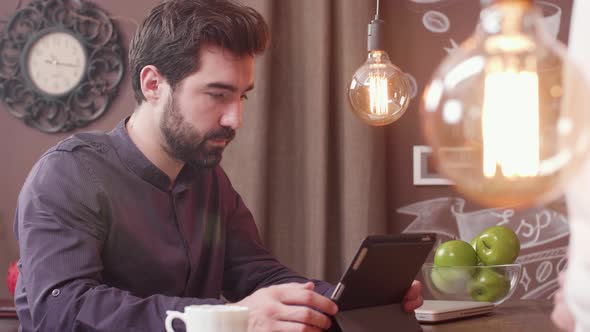Young Bearded Man Using a Tablet at a Bar Counter alt