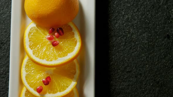 Slice of orange with pomegranate seeds in tray on black background 4K 4k alt