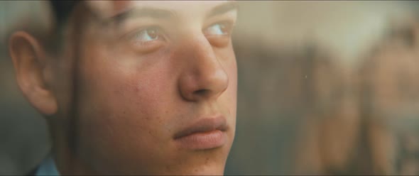 Closeup of the face of a young man staring up hopeful through the window alt