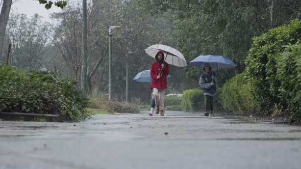 Three kids running happy in the rain and puddles with umbrellas alt