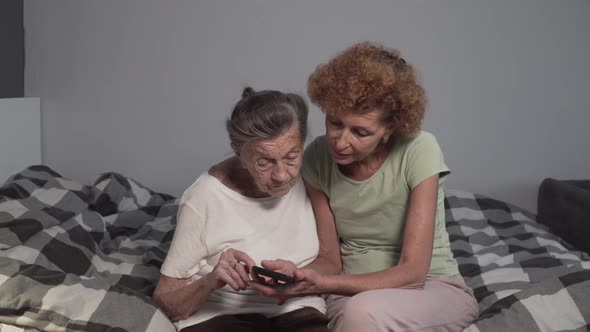 Mature Daughter Visits Senior Mother in Nursing Home and Teaches How To Use Smartphone alt