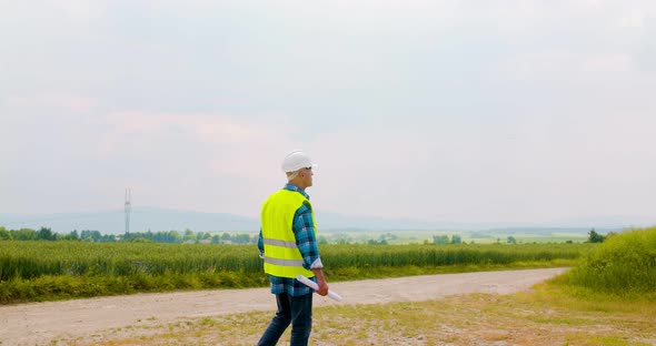 Engineer with Blueprint Analyzing Farm Against Sky alt