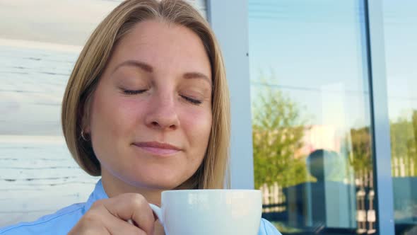 A Beautiful Woman with Blue Eyes Drinks Coffee in the Morning on the Terrace of Her House Looks Into alt