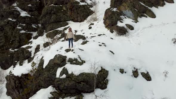 A Tourist Girl in a Warm Jacket and Boots Stands on Top of a Snowy Mountain