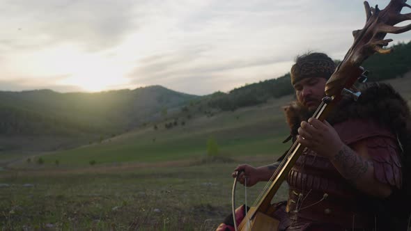 Large Man in Shaman Costume Plays Ikili Sitting in Valley alt