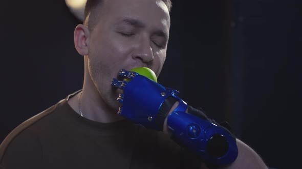 A Disabled Man with a Prosthetic Hand is Biting a Green Apple