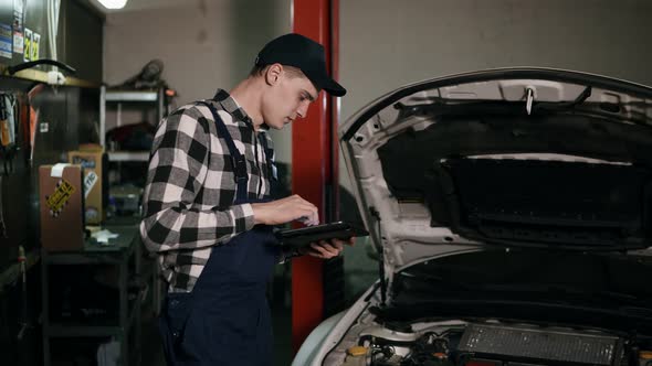 Mechanic Inspects the Car Undercarriage Way with a Digital Tablet alt