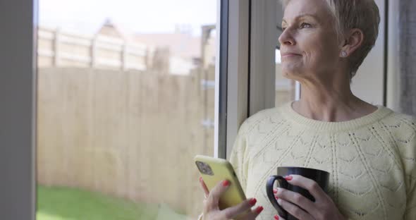 Mature woman holding coffee cup using smartphone