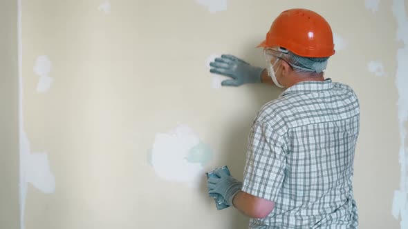 An Elderly Man Master Levels a Wall with a Tool in an Orange Helmet and Protective Glasses While