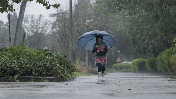 Slow motion of a little girl skipping in puddles holding an umbrella in the rain alt