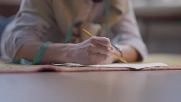 Unrecognizable Man Lying on Floor Drawing Clothes Sketch with Pencil alt