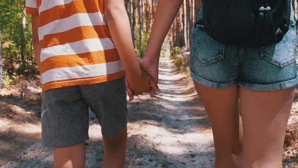 Young Mother and Son Holding Hands Walking Along a Path in Forest. Slow Motion alt