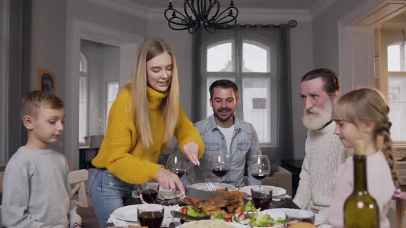 Woman Carving Tasty Roast Turkey for Her Relatives which Sitting at the Festive Family Table alt