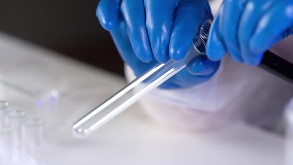 Close-up of medical scientist pouring dark liquid solution into tube. alt