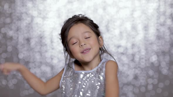 Beautiful Smiling Little Child Girl in a Silver Dress Dancing on Background of Silver Bokeh