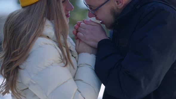 Closeup Boyfriend Warming Girlfriend Hands with Breathe Standing in Sunny Winter Forest Smiling alt