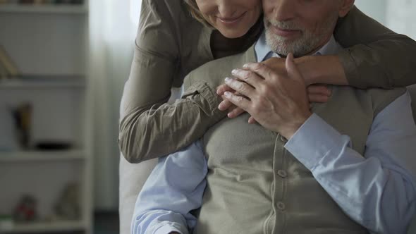 Male Retiree Reading Newspaper, Female Hugging from Behind, Loving Tenderness alt