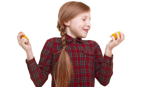 Cute Smiling Caucasian Girl Holding Two Halfs of Orange Smelling with Excitement and Biting It alt
