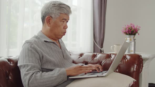 Senior man typing chatting on laptop computer in living room