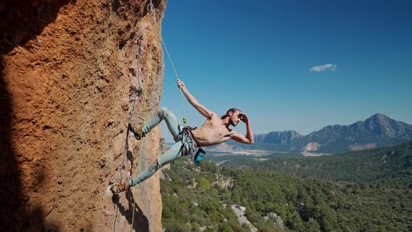 Strong and Muscular Fit Rock Climber Hangs on Rope on Vertical Cliff alt