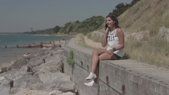 A Young Attractive Woman Sits By The Sea And Receives A Call From A Close Friend - Ungraded alt