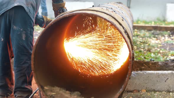 The Welder Cuts a Large Diameter Metal Pipe and Sparks Fly