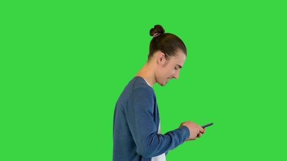 Young White Man Walks Typing Something on His Smartphone on a Green Screen Chroma Key