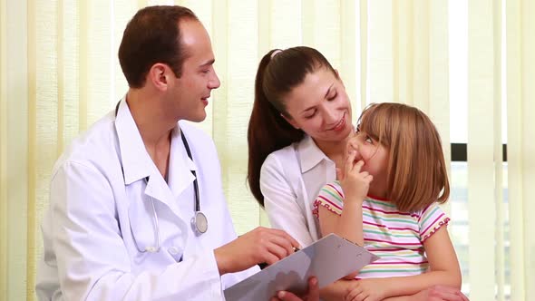 Doctor talking to a girl while she sits on the knees of her mother alt