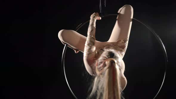 Portrait of Slim Young Woman Performing Acrobatic Tricks on Air Hoop at Black Background alt