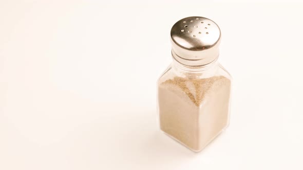 Glass Pepperjar with Stainless Steel Cap Full of Grounded Black Peppercorns Spinning on White alt