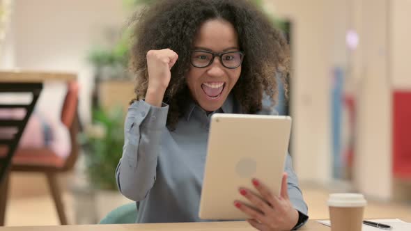 Young African Woman Celebrating on Tablet at Work alt