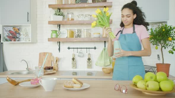 Young Woman Is Putting Flowers in a Vase and dancing at the Kitchen alt