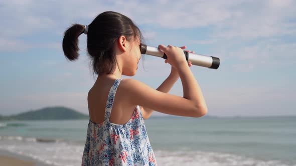 Asian child girl looking in spyglass, Happy kid playing outdoors on the beach