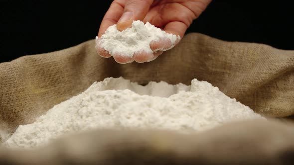 Human hand takes a pinch of a wheat powder from a top of pile in a sac