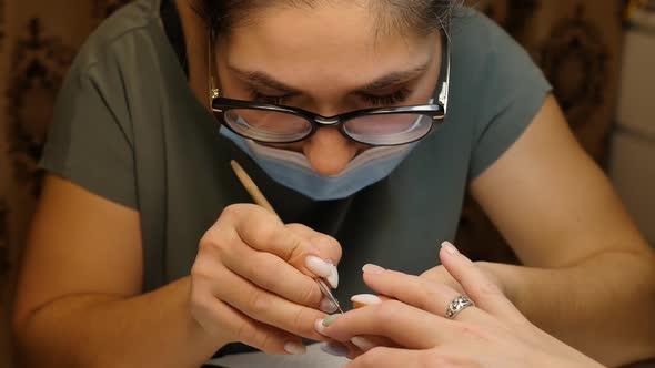 Manicurist Woman of Oriental Nationality in Glasses Applies Varnish on a Nail